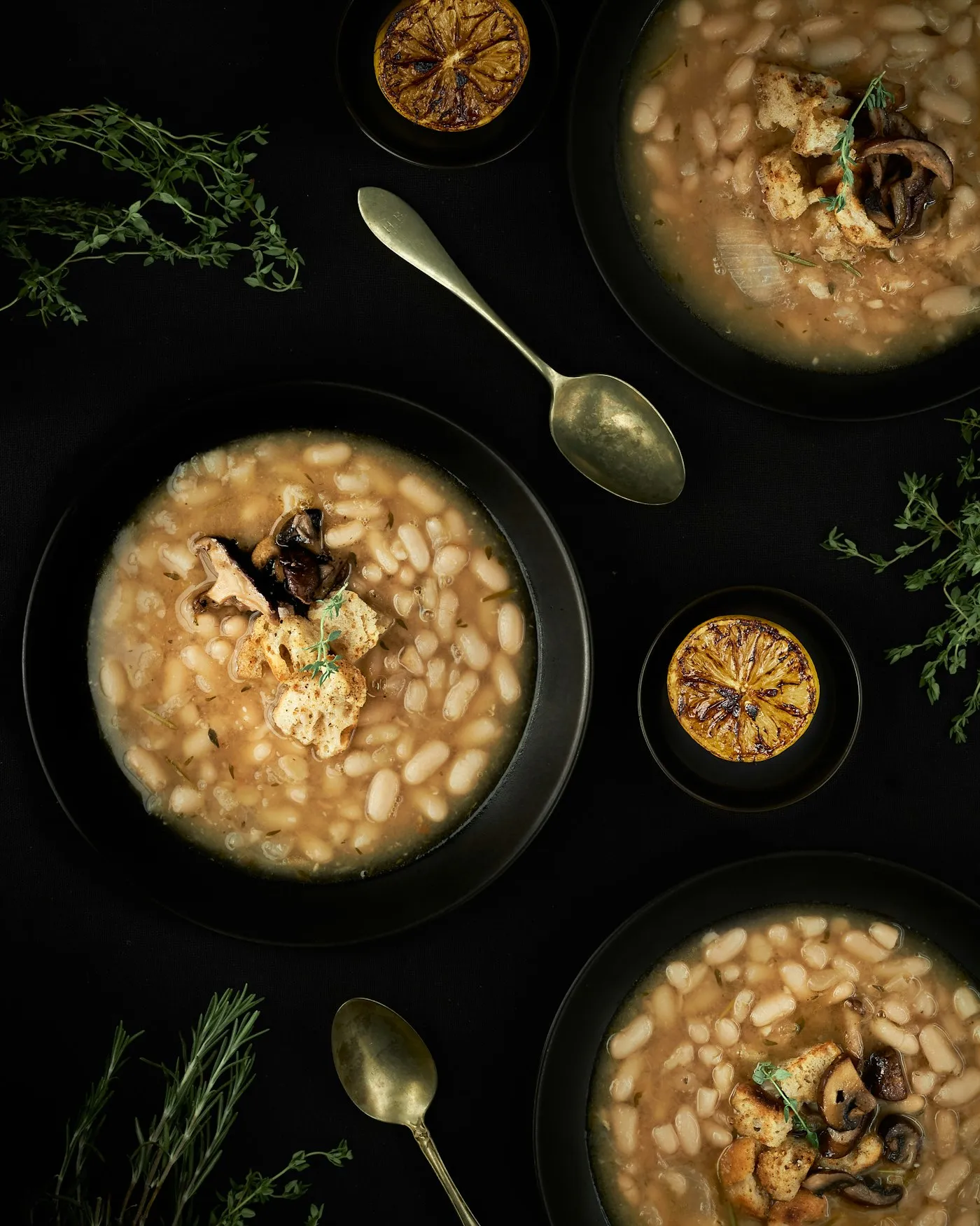 A dark ceramic bowl of pale bean stew, photographed from above