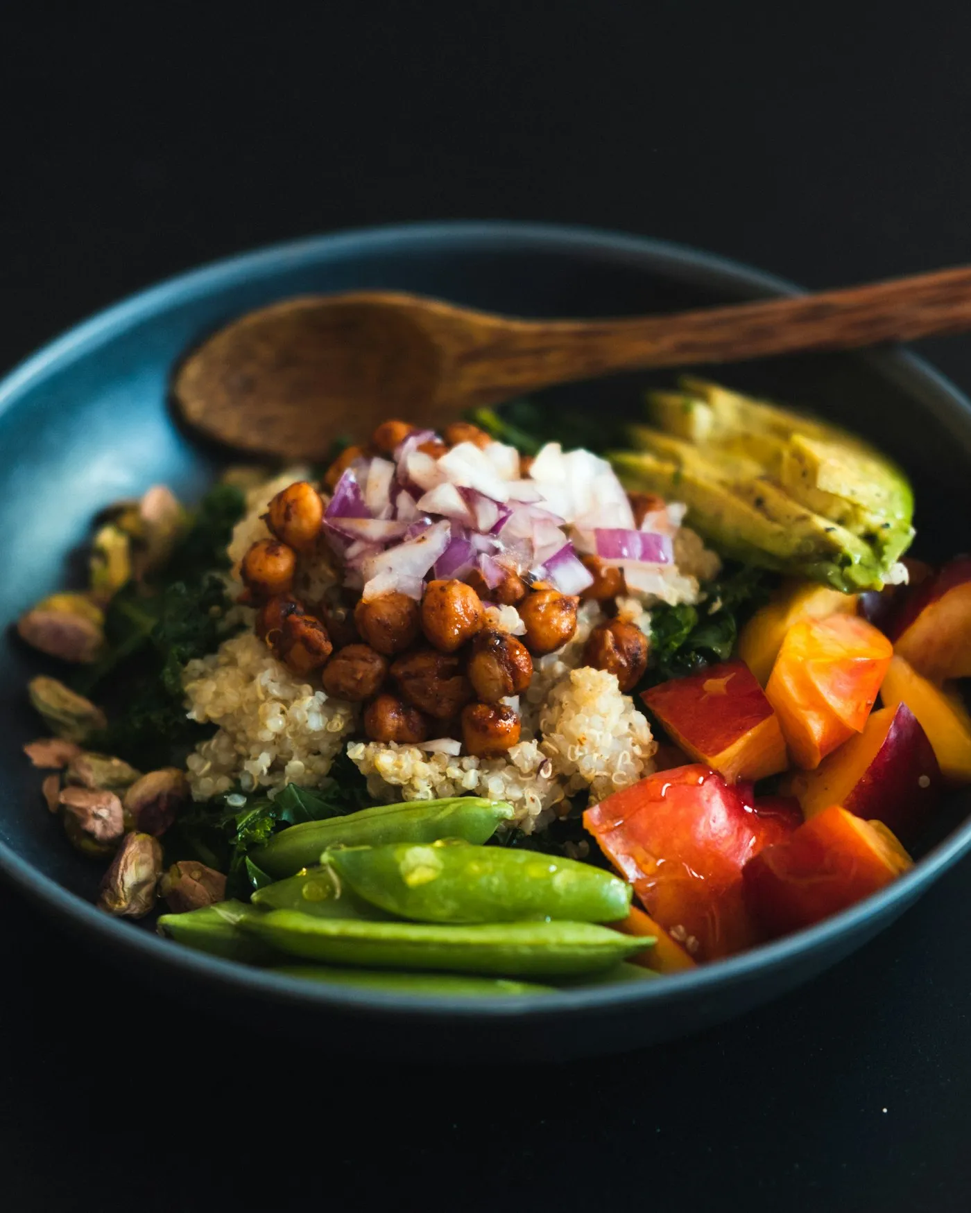 A blue bowl filled with chickpeas and vegetables, with a wooden spoon