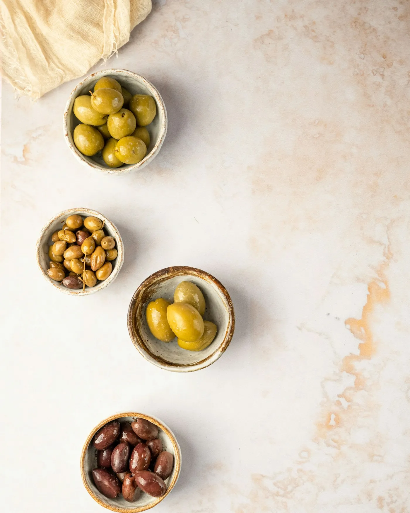 Three small bowls of olives on a table with a linen cloth