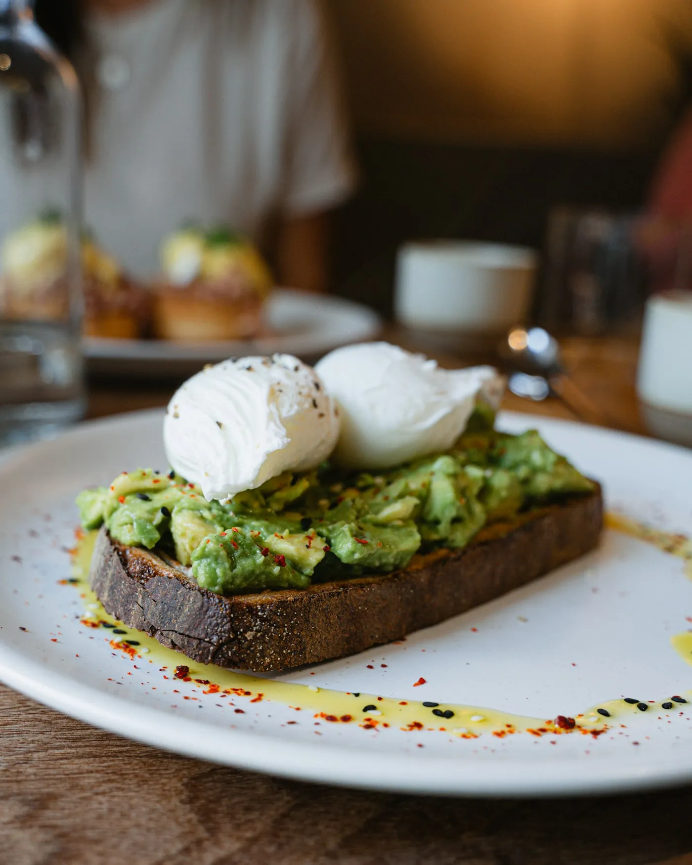 A white plate with a thick slice of toast piled with crushed avocado