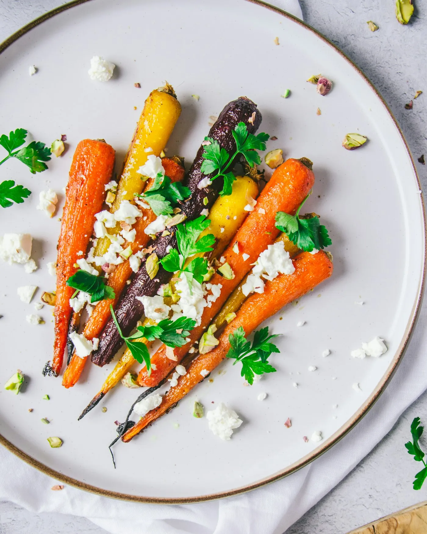 A white plate of roasted carrots with crumbled cheese and herbs