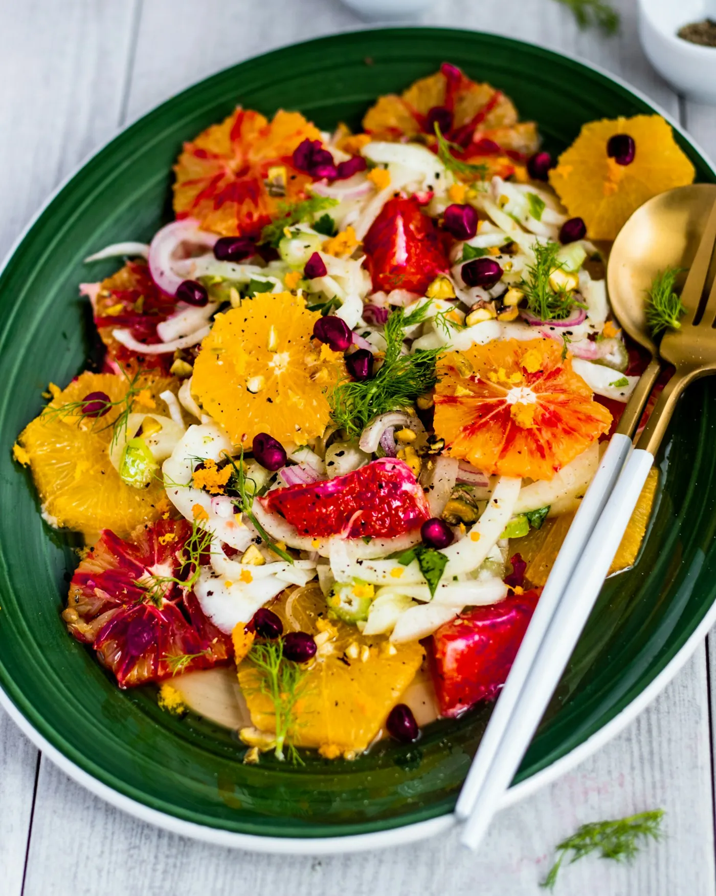 A green plate holding a salad of shaved vegetables and citrus segments