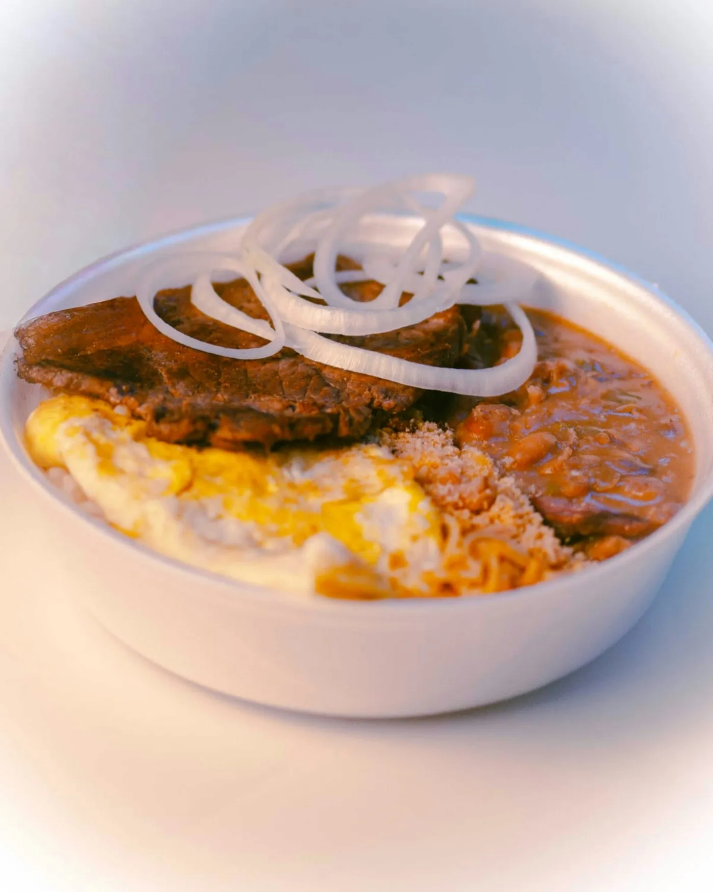 A bowl of rice topped with meat, fried eggs and sliced onions