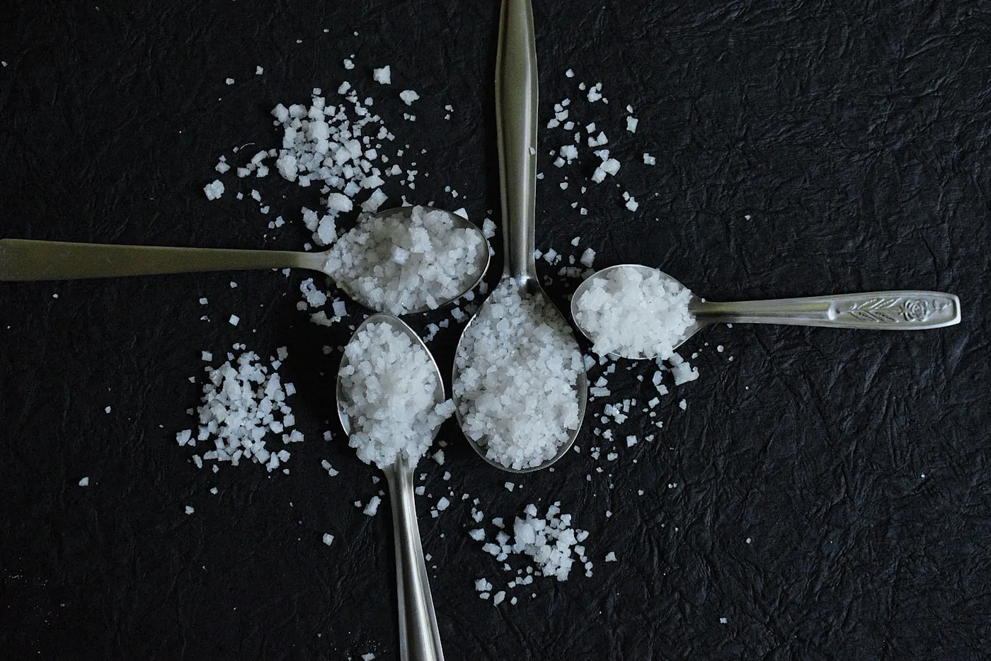 Four spoons of salt on a dark surface