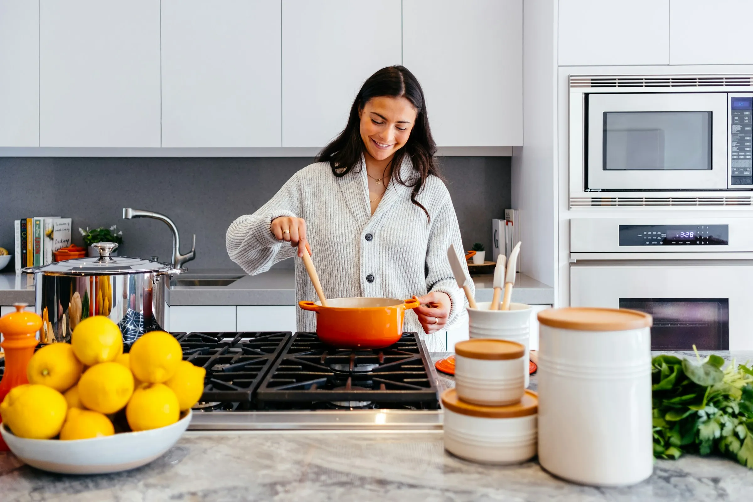 A woman stirring an orange pot on the hob in a bright white kitchen